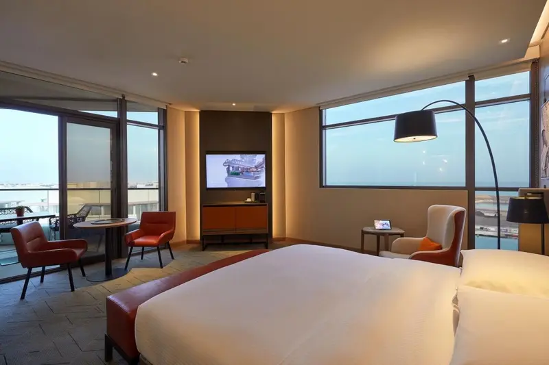 Chambre lumineuse avec un grand lit et un coin salon près des fenêtres.