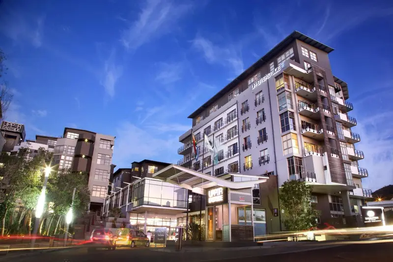 Bâtiment moderne illuminé au crépuscule avec des balcons et des arbres en premier plan.