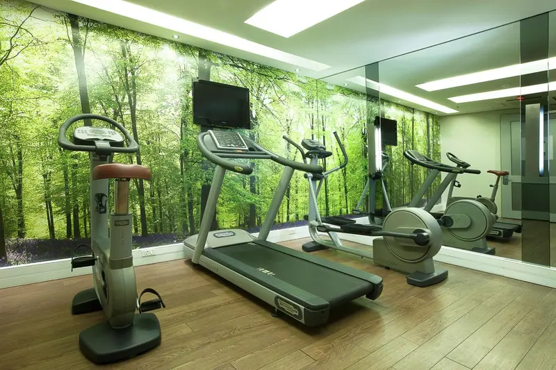 Une salle de sport lumineuse avec des équipements de cardio et un décor mural forestier.