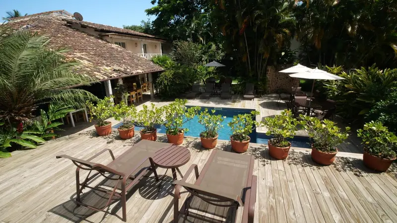 Terrasse en bois avec transats et piscine entourée de végétation tropicale.
