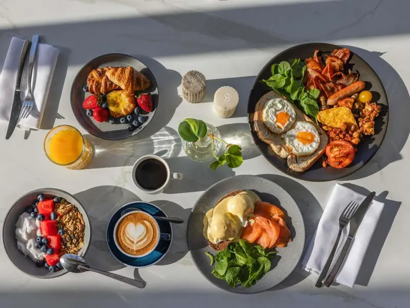 Assiettes garnies de viennoiseries, de fruits, d'oeufs et de boissons sur une table.