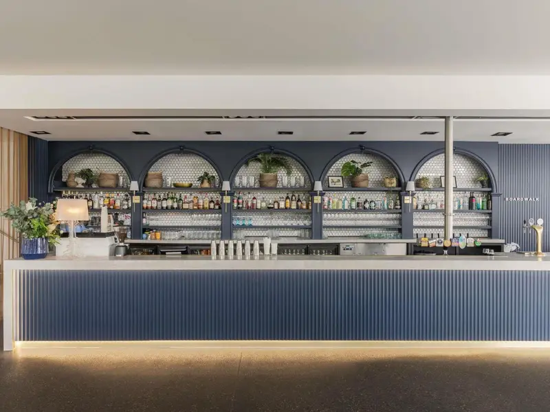 Un comptoir de bar moderne avec une étagère remplie de bouteilles et de verres.