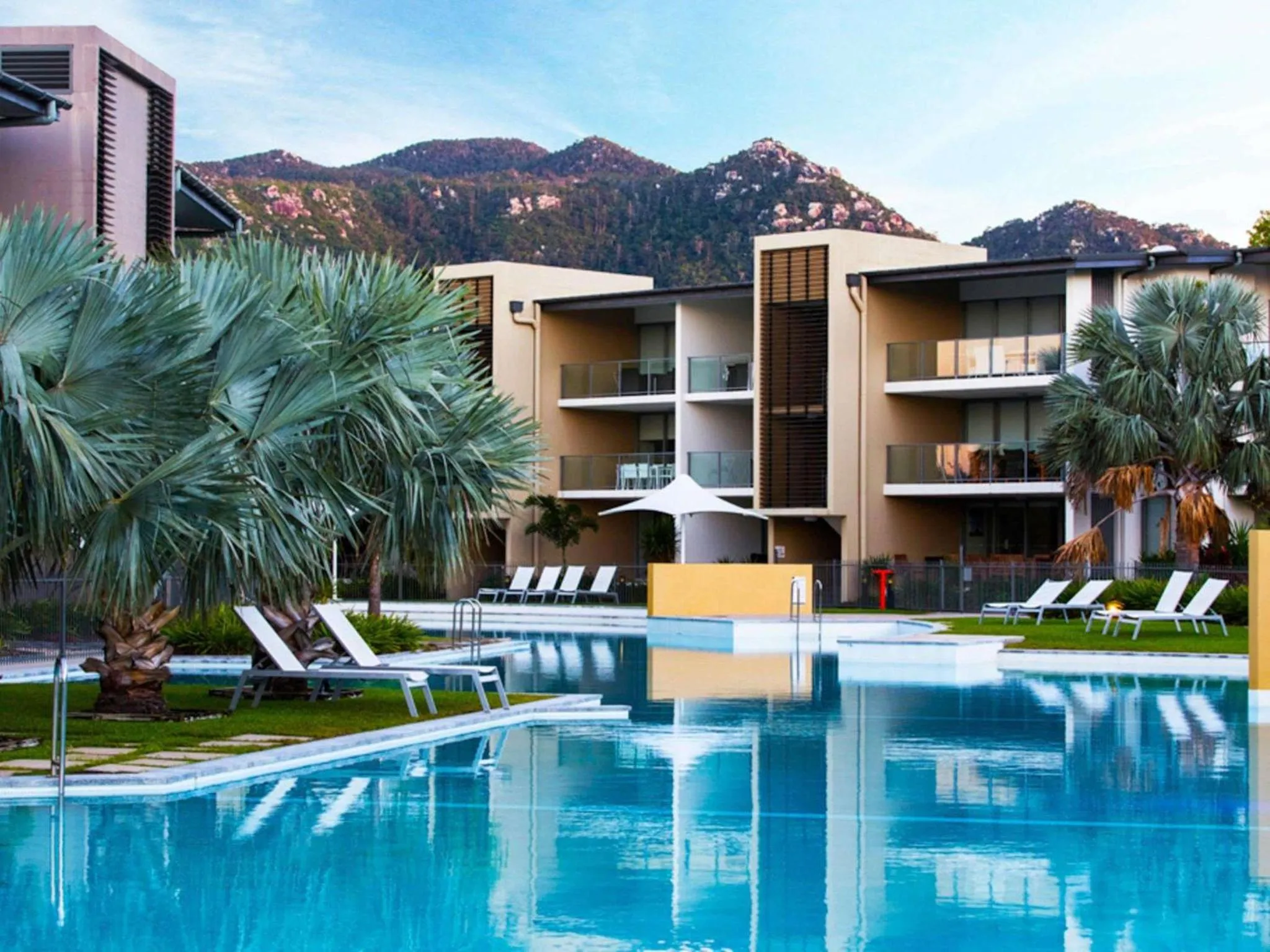 Vue d'une piscine devant un bâtiment moderne avec des transats.