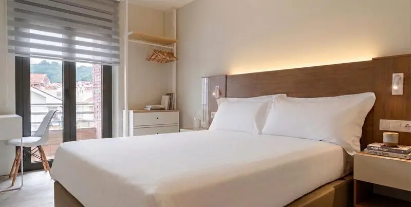 Une chambre lumineuse avec un lit double et un bureau près d'une fenêtre.