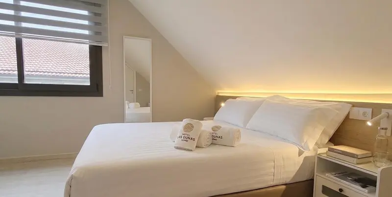 Une chambre lumineuse avec un grand lit blanc et une fenêtre.
