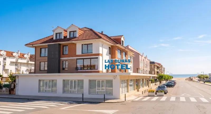 Façade d'un bâtiment blanc et beige avec des fenêtres et un toit rouge, bordant une rue.
