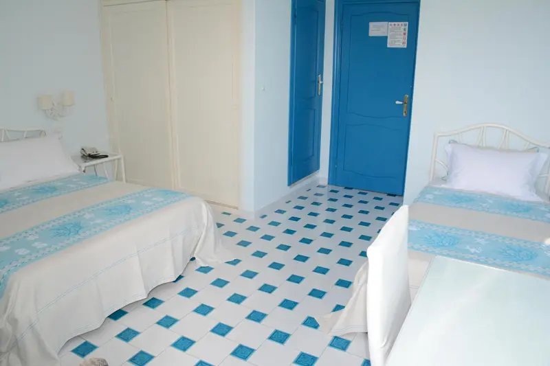 Une chambre lumineuse avec deux lits simples et un carrelage bleu.