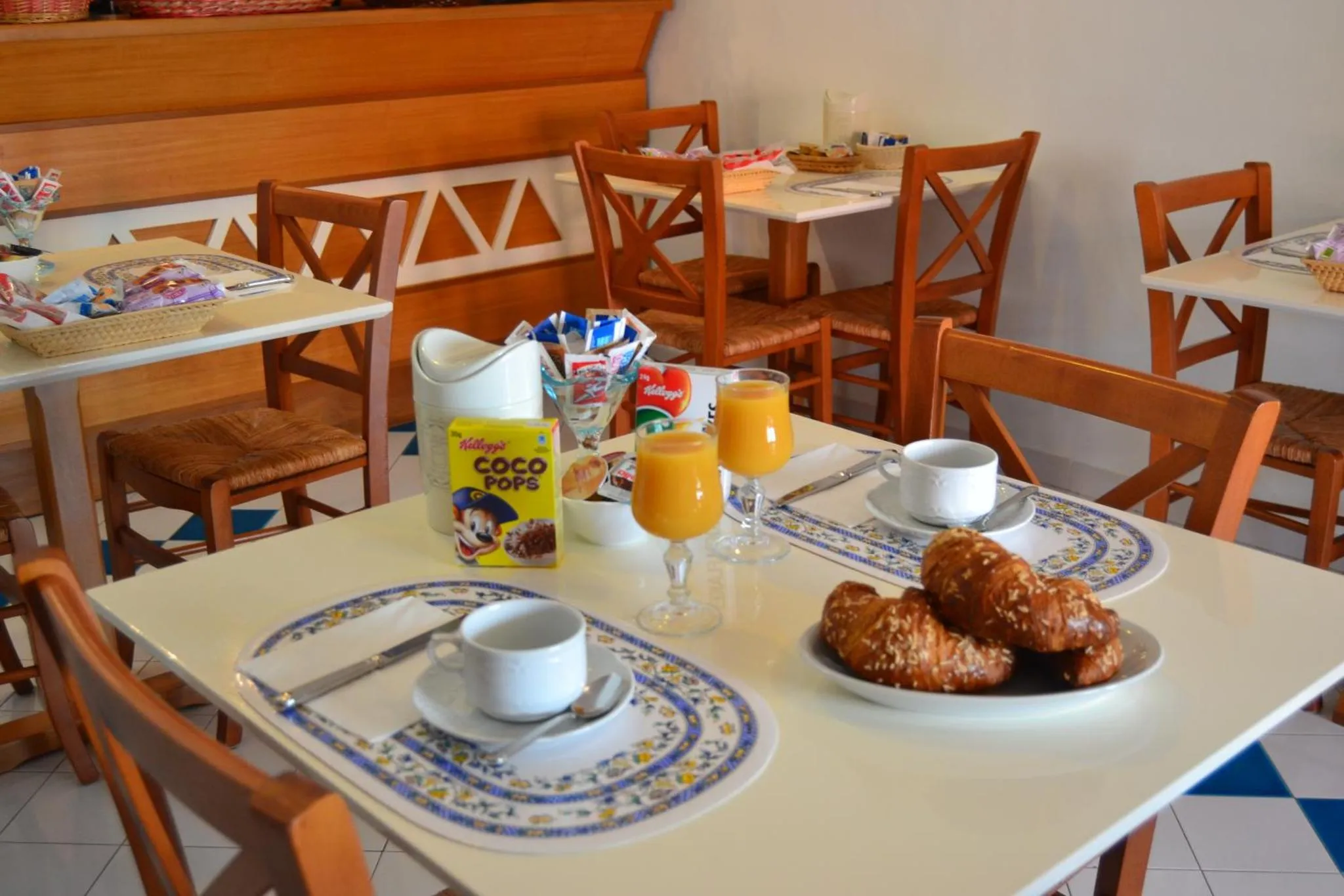 Une table est dressée pour le petit-déjeuner avec des viennoiseries et des boissons.