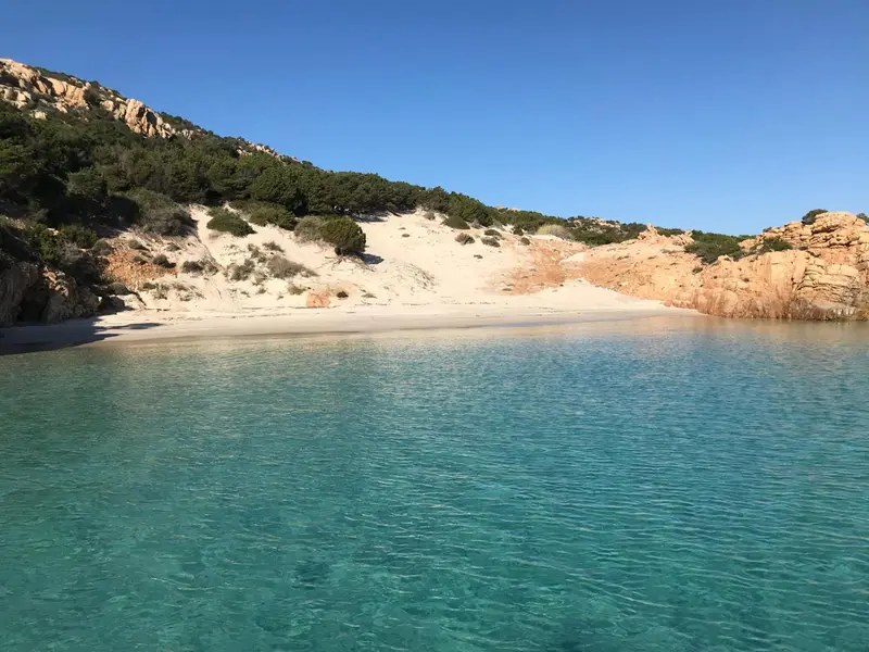 Une plage de sable blanc bordée d'une eau turquoise et de collines verdoyantes.