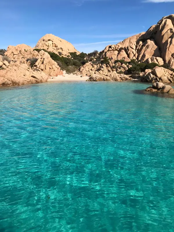 Une plage de sable blanc bordée d'une eau turquoise et de rochers rouges.