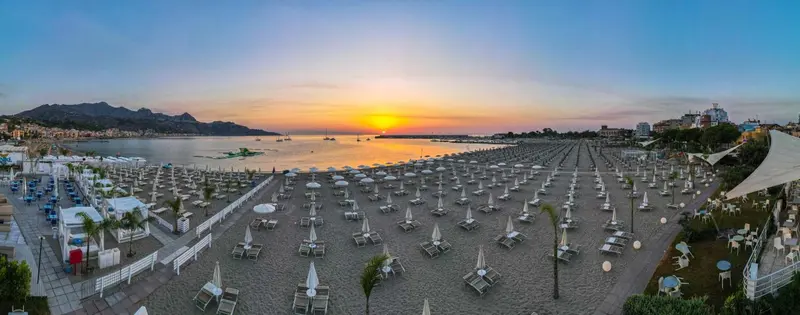 Vue aérienne d'une plage de sable avec des transats et des parasols au coucher du soleil.