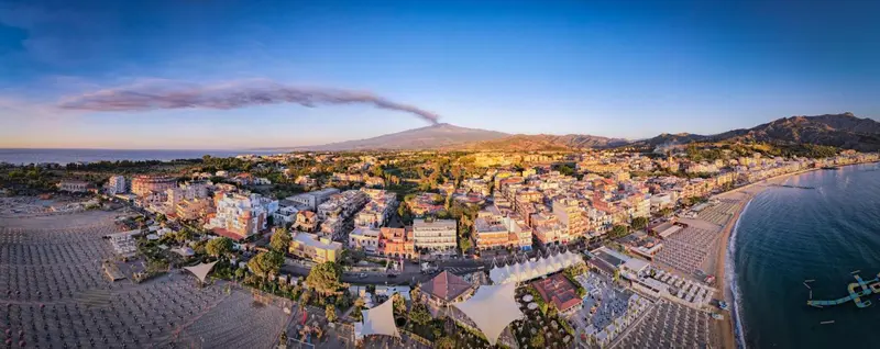 Vue aérienne d'une station balnéaire avec une plage et un volcan en arrière-plan.