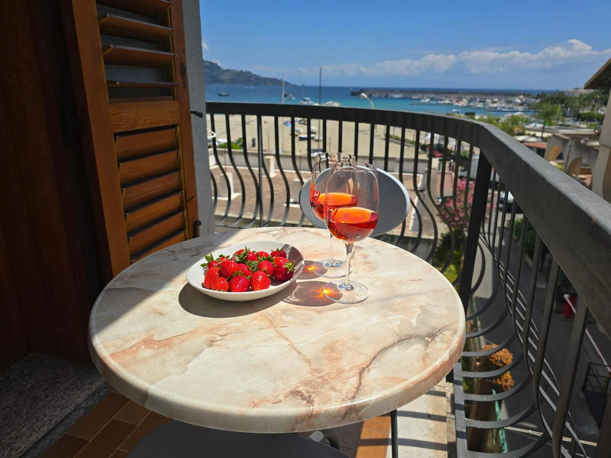 Une table ronde avec des fruits et des verres sur un balcon ensoleillé avec vue sur la mer.