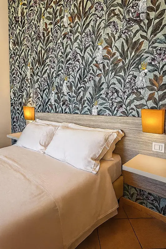 Lit double avec oreillers blancs dans une chambre décorée de papier peint floral.