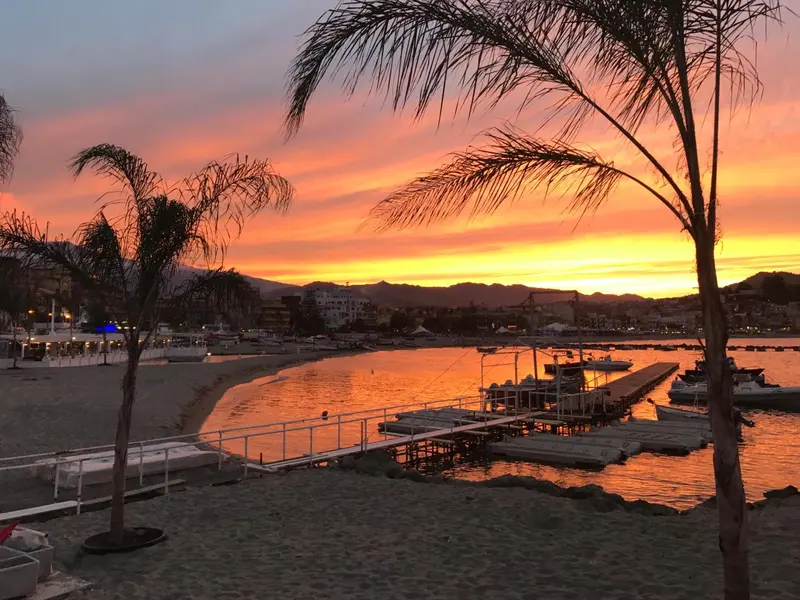 Coucher de soleil sur une plage avec des palmiers et des bateaux amarrés.