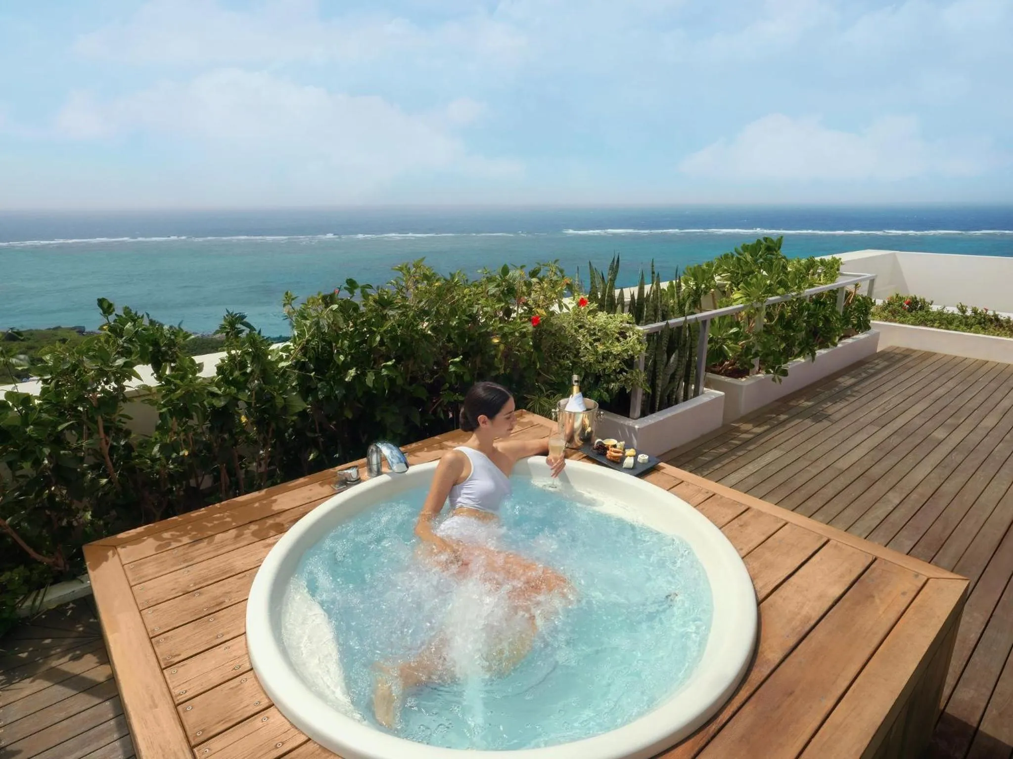 Une femme se détend dans un jacuzzi sur une terrasse avec vue sur la mer.