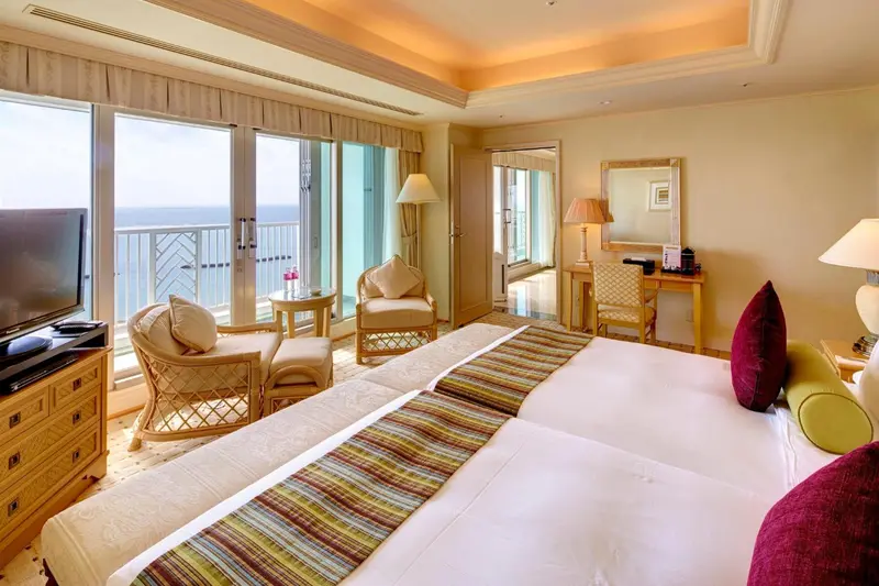 Une chambre lumineuse avec un grand lit et un accès à un balcon donnant sur la mer.
