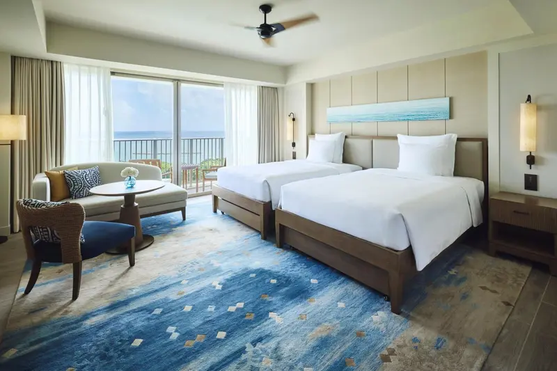Chambre lumineuse avec deux lits et vue sur la mer.