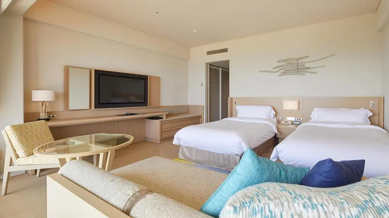 Une chambre lumineuse avec un canapé, une télévision et deux lits simples.