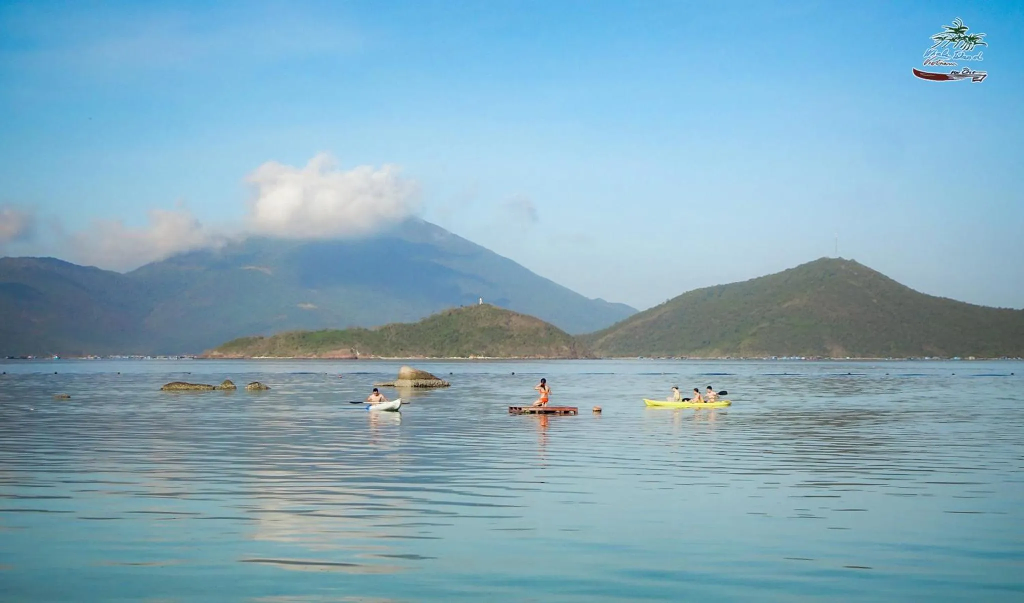 Des personnes se détendent sur des planches de paddle dans une eau turquoise face à des îles verdoyantes.