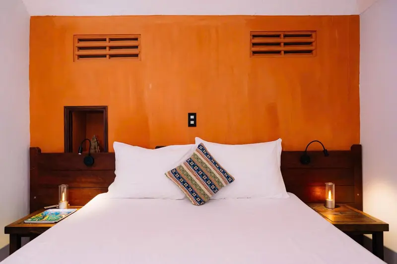 Un lit blanc avec des oreillers dans une chambre aux murs orange et bois.