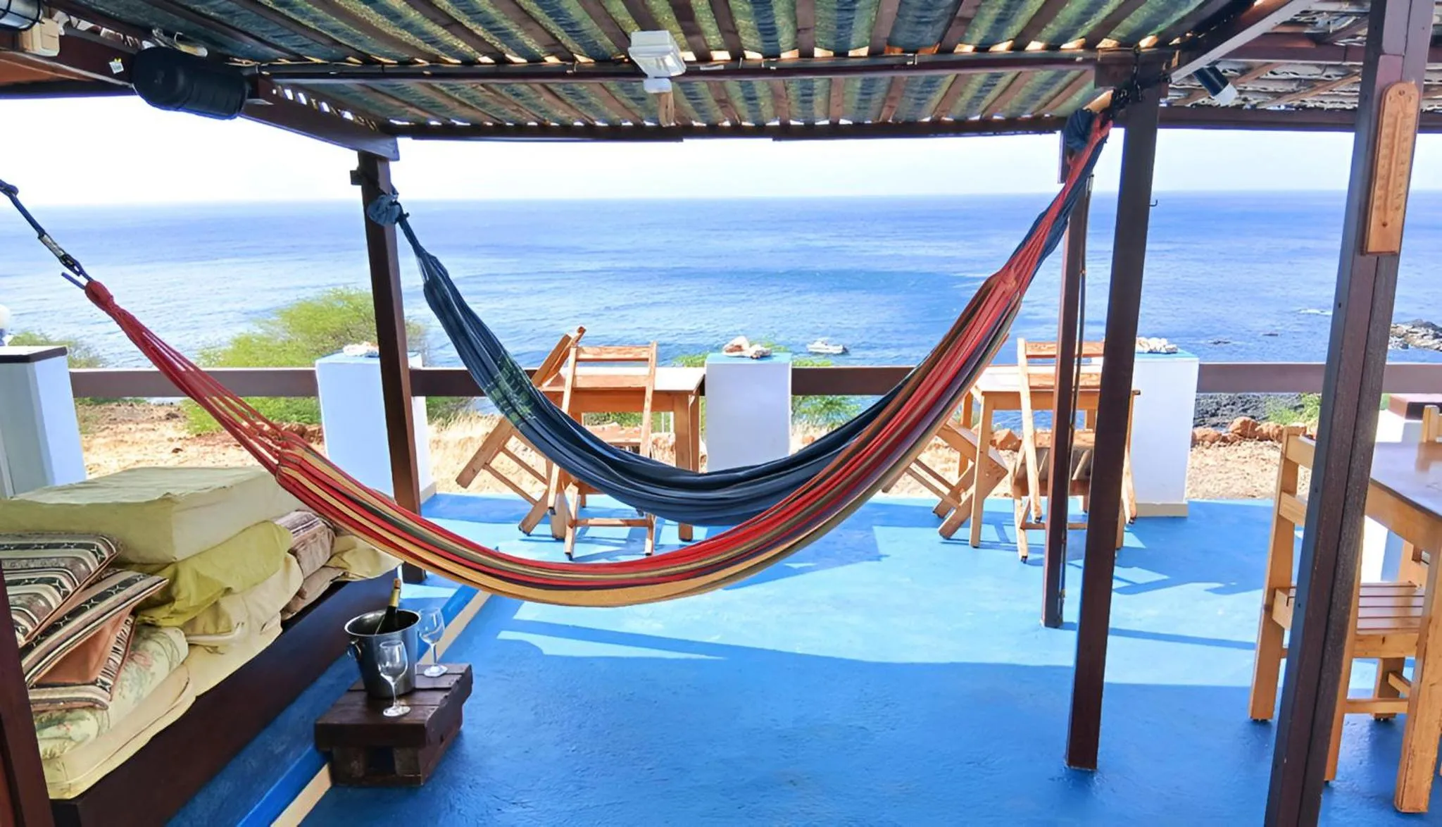 Un hamac coloré est suspendu sur une terrasse bleue avec vue sur la mer.