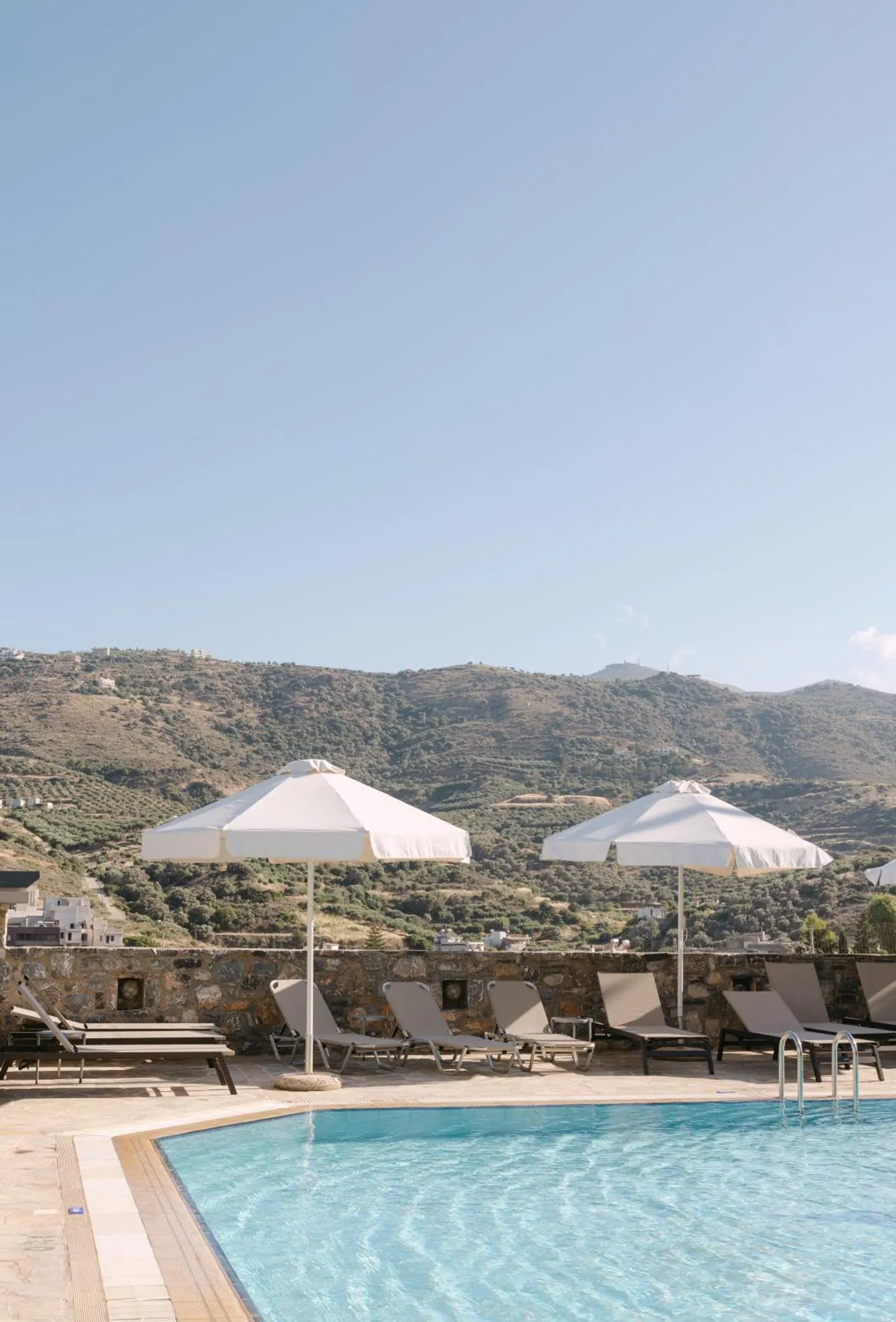 Transats blancs disposés autour d'une piscine avec vue sur des collines.