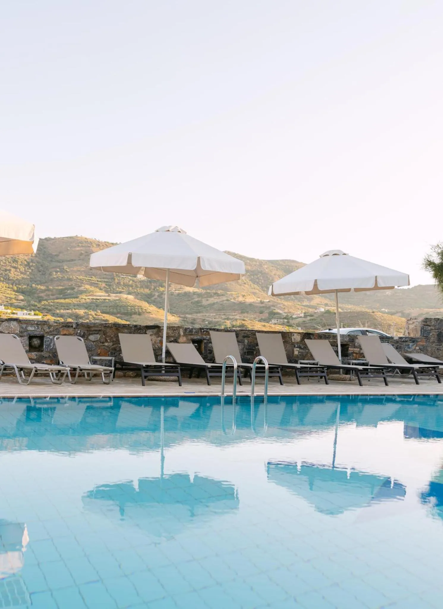 Transats et parasols bordent une piscine turquoise reflétant le ciel.