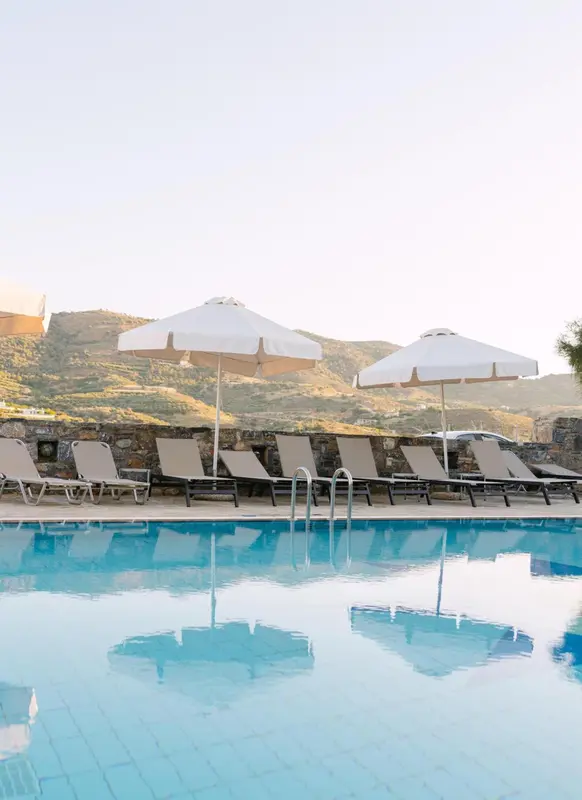 Transats et parasols bordent une piscine turquoise reflétant le ciel.