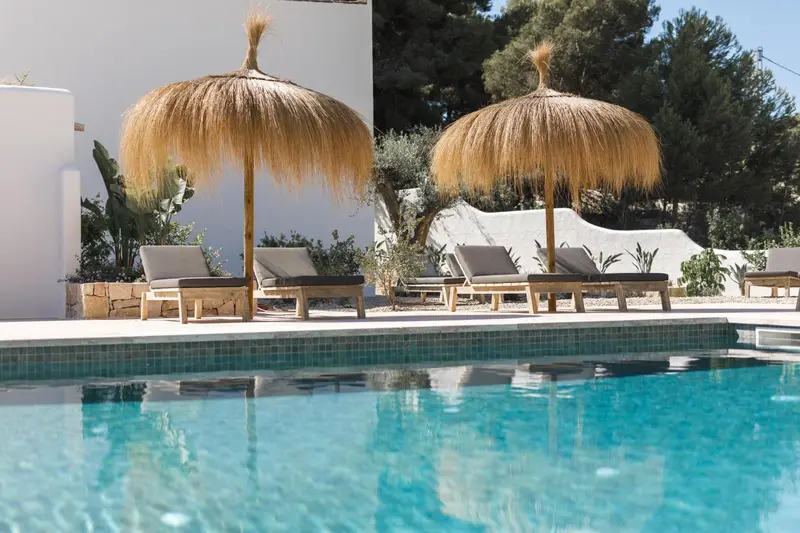 Transats et parasols en chaume bordent une piscine turquoise.