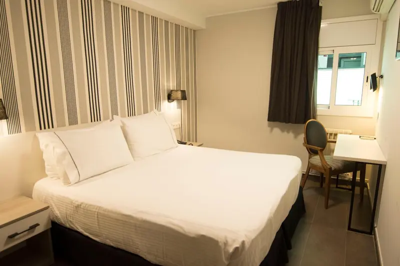 Une chambre avec un lit double et un bureau près d'une fenêtre.