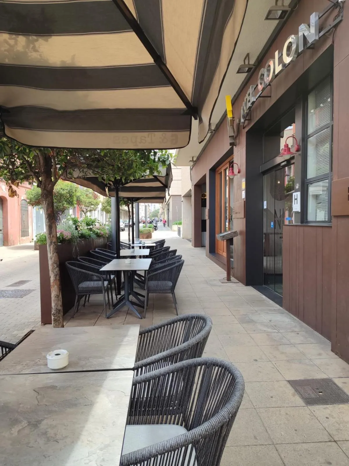 Terrasse ombragée avec tables et chaises en osier devant un bâtiment.