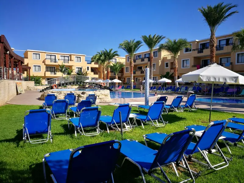 Transats bleus disposés sur une pelouse verdoyante devant une piscine et un bâtiment.