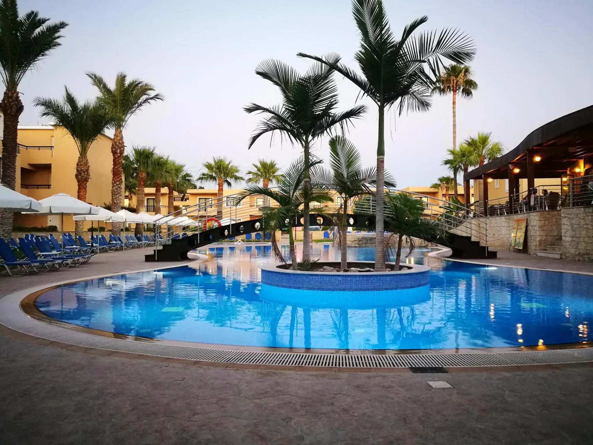 Piscine extérieure avec transats et végétation tropicale au crépuscule.