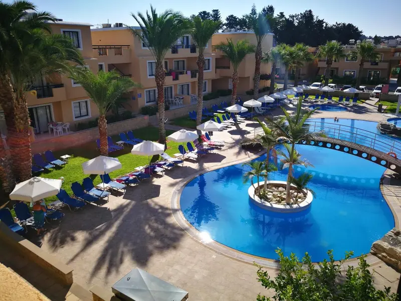 Vue aérienne d'une piscine entourée de transats et de palmiers devant un bâtiment.