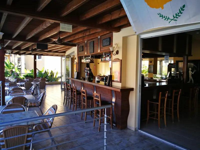 Un bar extérieur avec des tabourets et des tables, ouvert sur une salle intérieure.