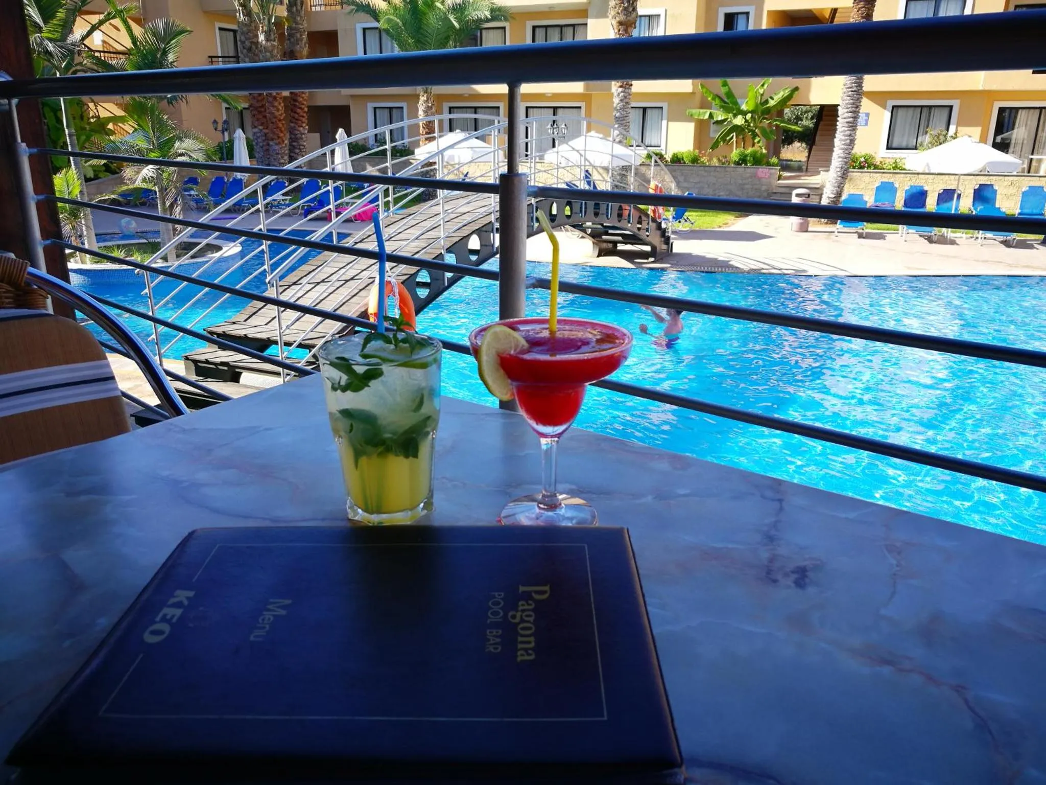 Deux cocktails colorés sont servis sur une table près d'une piscine ensoleillée.