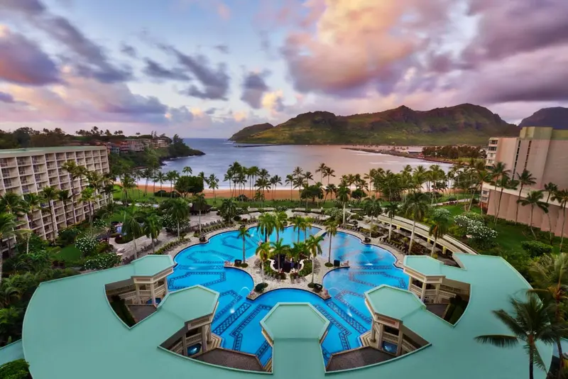 Vue aérienne d'un complexe hôtelier avec piscine et plage au coucher du soleil.