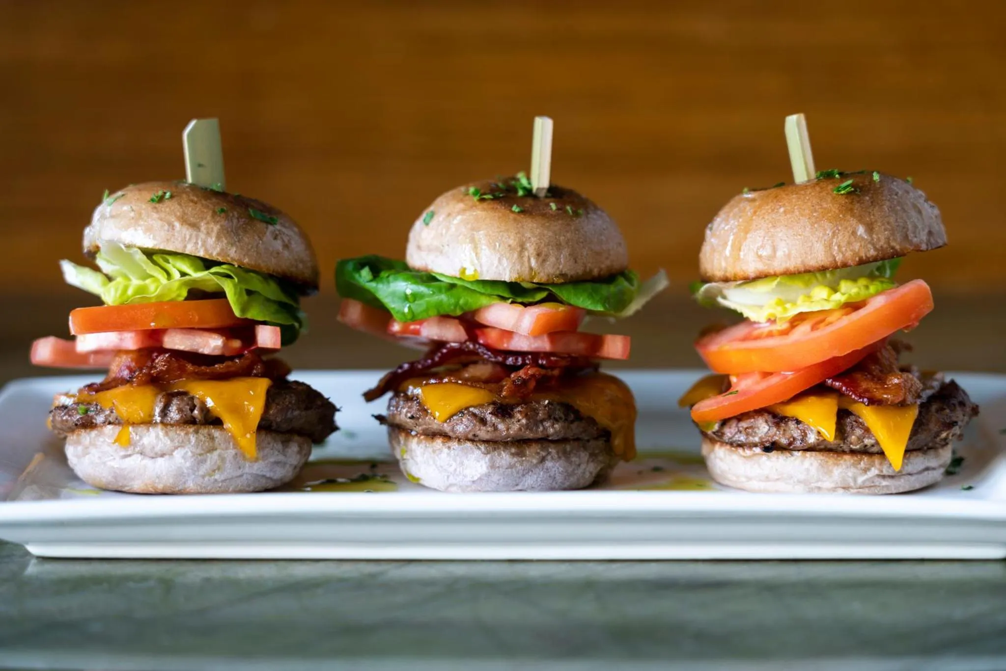 Trois mini-burgers alignés sur une assiette blanche.