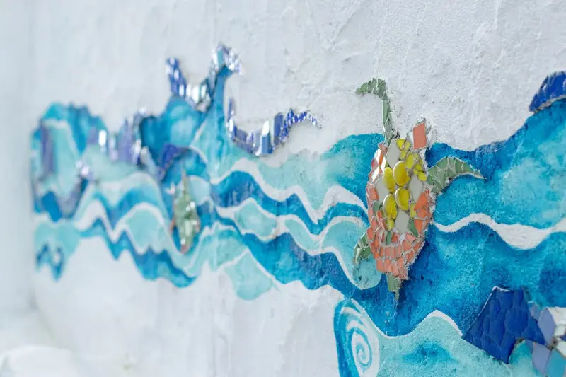 Une mosaïque représentant des vagues et une tortue marine orne un mur blanc.