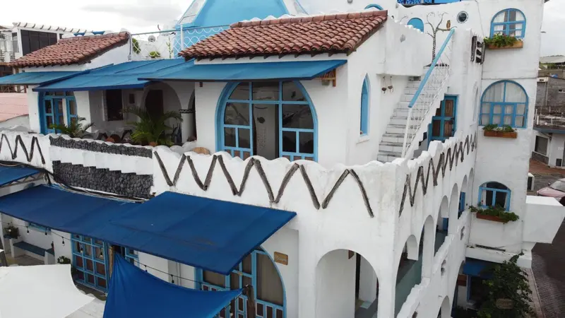 Bâtiment blanc aux fenêtres et balcons bleus, avec des toits en tuiles rouges.
