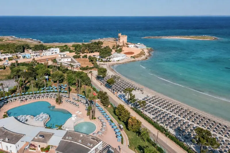 Vue aérienne d'une plage bordée de transats et d'une piscine d'hôtel.