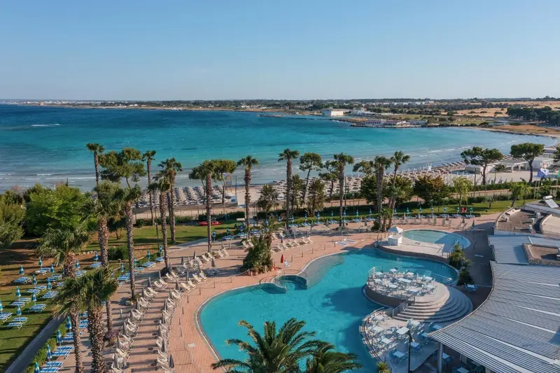 Vue aérienne d'une piscine et d'une plage bordée de palmiers.