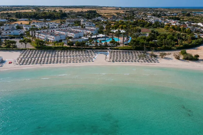 Vue aérienne d'une plage de sable blanc bordée de transats et d'un complexe hôtelier.
