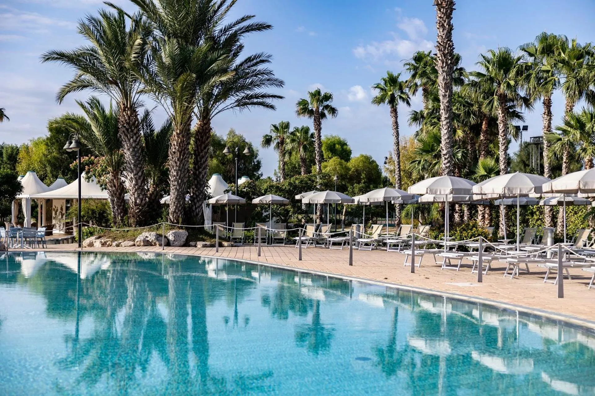 Transats et parasols bordent une piscine turquoise reflétant les palmiers.
