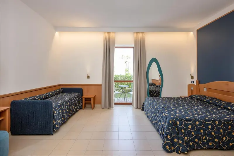 Une chambre lumineuse avec deux lits et un canapé face à une porte-fenêtre.