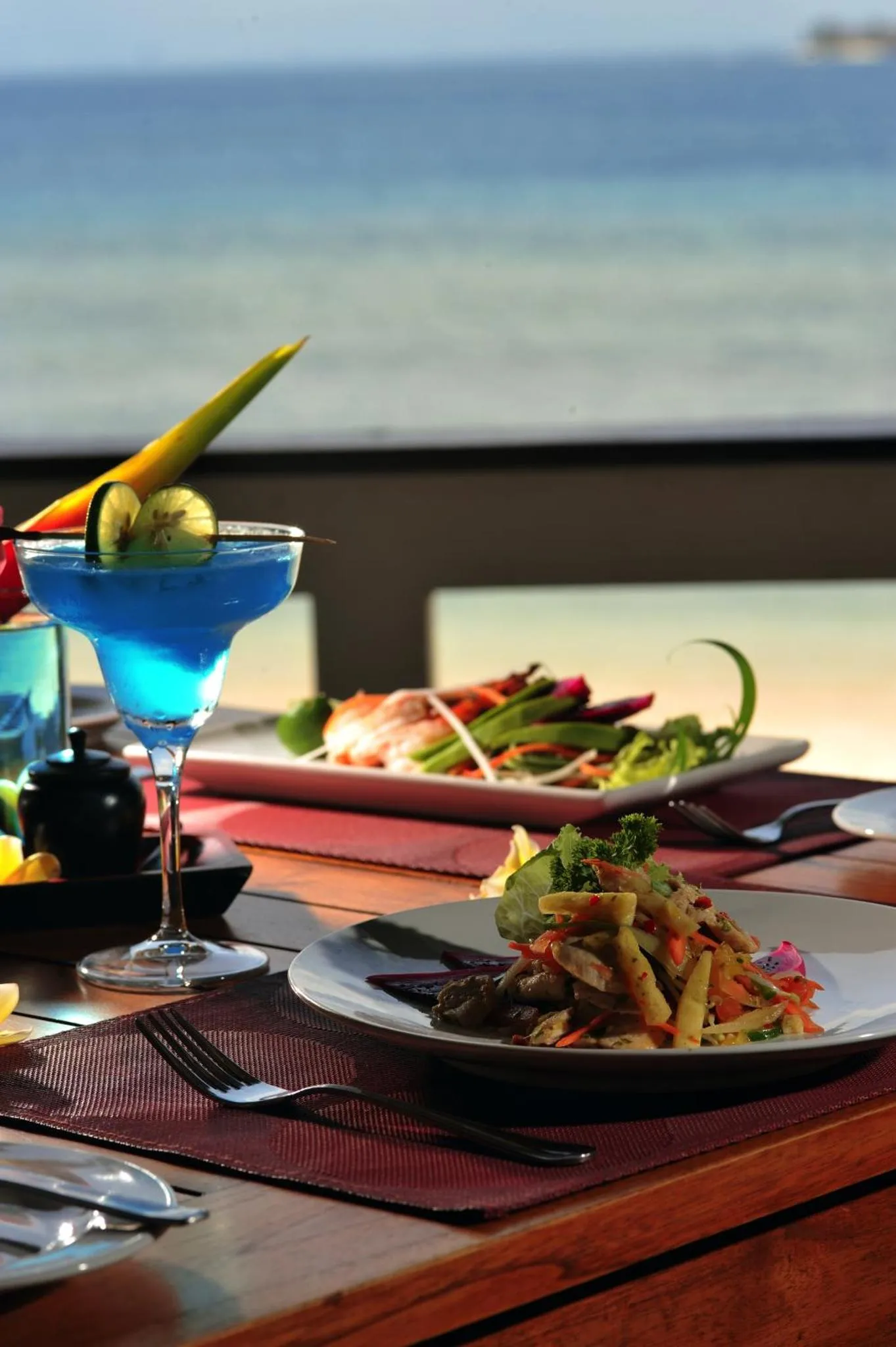 Une table est dressée avec des plats colorés et une boisson rafraîchissante en bord de mer.