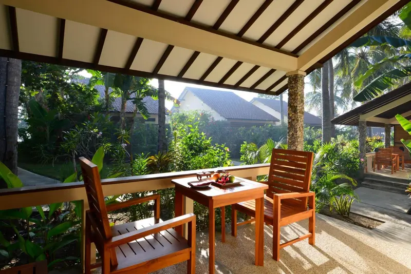 Une table et des chaises en bois sont disposées sur une terrasse ombragée.