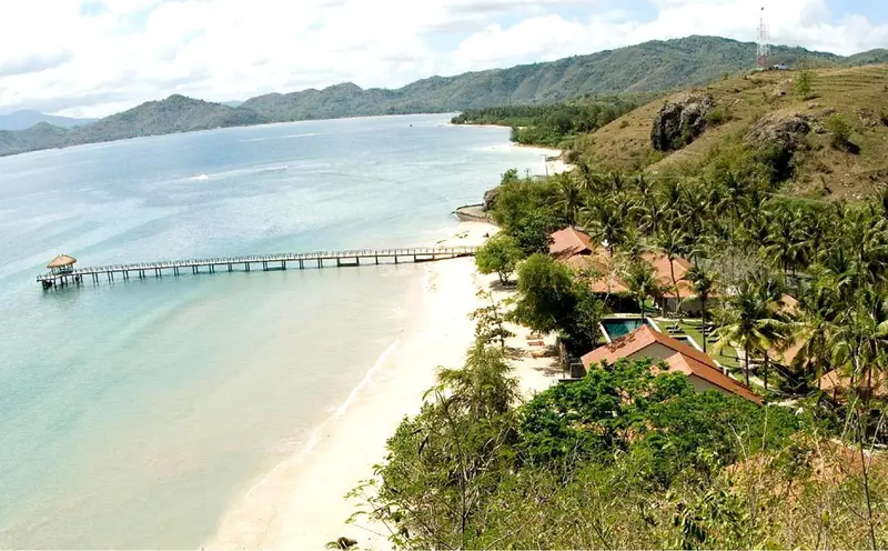 Vue aérienne d'une plage de sable blanc bordée de bâtiments et de végétation tropicale.