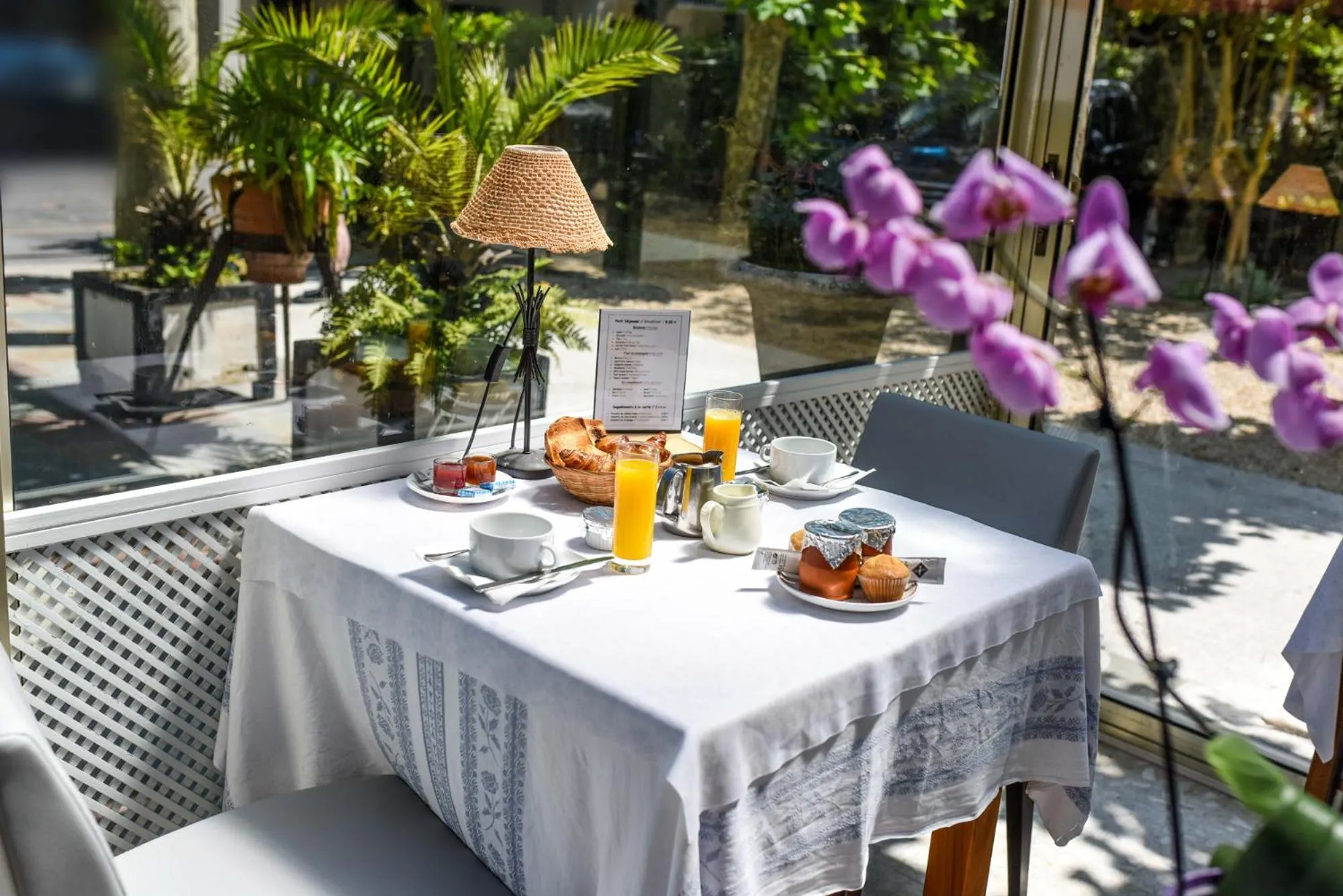 Une table est dressée avec un petit-déjeuner composé de viennoiseries, de jus d'orange et de boissons chaudes.